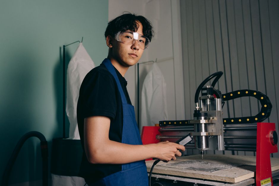 安全眼鏡を着用したアジア系エンジニアがCNC機械で作業している。屋内の産業環境。