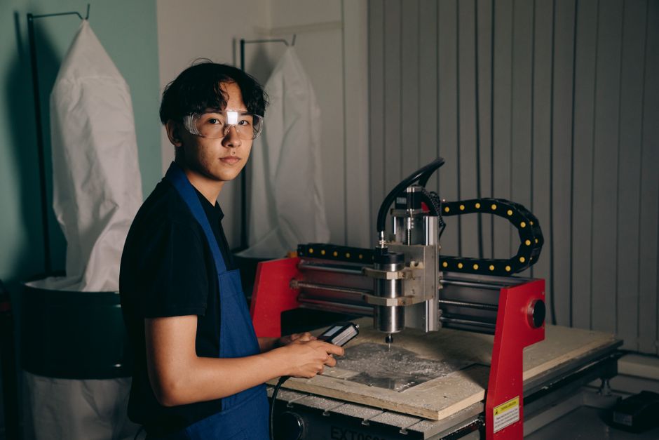 作業場でCNC機械を操作している若い作業者のポートレート。保護メガネとエプロンを着用している。