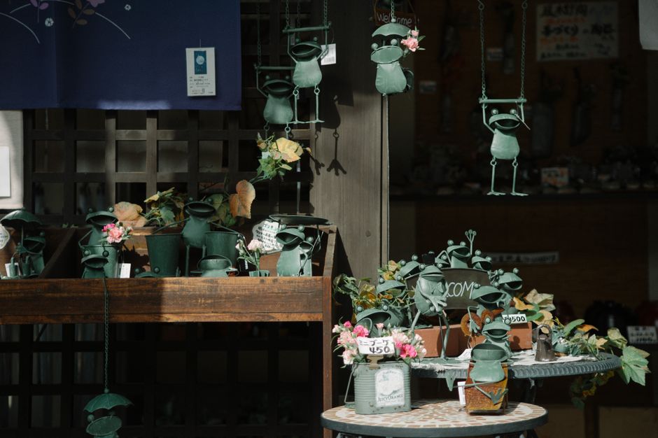 花と値札で飾られた日本のお店にある、風変わりなカエルの置物のコレクション。