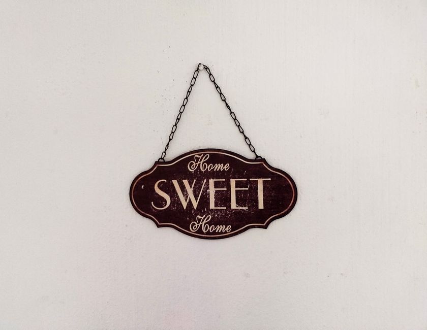 白い壁に掛かっているヴィンテージの'Home Sweet Home'サインのクローズアップ。