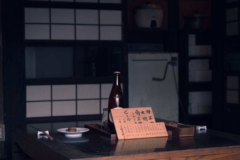 テーブル、日本酒の瓶、手書きのメニューカードが置かれた、居心地の良い和室。